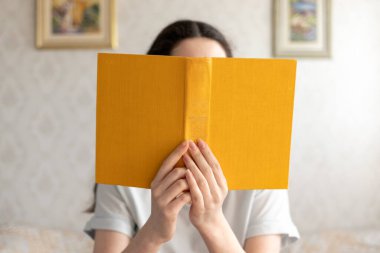 Genç bir kadın kitap okuyor, yüzünü onunla gizliyor. Eğitim ve Dünya Kitap Günü kavramı.