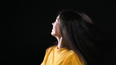 Genç, gülümseyen bir kadın başını farklı yönlere çevirir ve saçları alttan şişer. Siyah arka plan. Yavaş çekim
