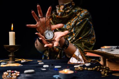 Falcı elinde zincirle bir saat tutuyor ve onu büyülüyor. Kehanet, astroloji ve geleceği tahmin etme kavramı..