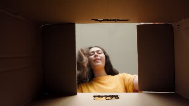 打开包装 一个笑着的年轻女人打开一个纸板箱 高兴地看着里面的东西 底部的观点 产品交付和转移概念 — 图库视频影像