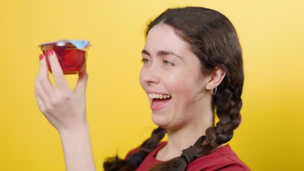 可愛い女の子の肖像画はゼリーの瓶を開き 試してみたいと思っています 黄色の背景 砂糖フリーデザート — ストック動画