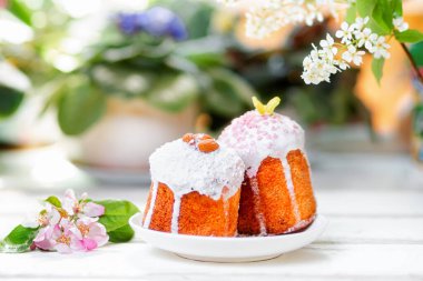 Paskalya Bayramı. Elma çiçeğinin yanındaki bir tabakta iki süslü Paskalya pastası. Arka planda bitkiler ve çiçekler. Yumuşak odak.