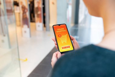 İnternet alışverişi. Bir kadının elinde online bir mağazada açık sayfası olan bir akıllı telefon var. Omzunun üstünden yakın çekim görüntüsü.