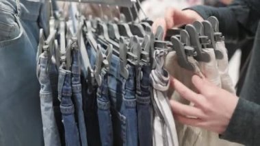 Kadının elleri, kot şortlu askılıkları birbirine yaklaştırıyor ve sevdiği modeli çıkarıyor. Gerçek zamanlı olarak. Tüketim ve alışveriş kavramı.