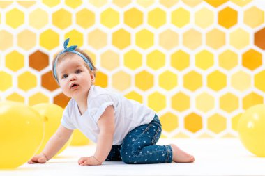 Sarı balonlarla yerde sürünen bir kız çocuğu. Arka planda sarı bal petekleri var. Dünya Çocuk Günü.