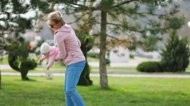 Anne çocukla oynuyor, onu kollarında sallıyor. Açık havada. Ağır çekim. Gerçek zamanlı..