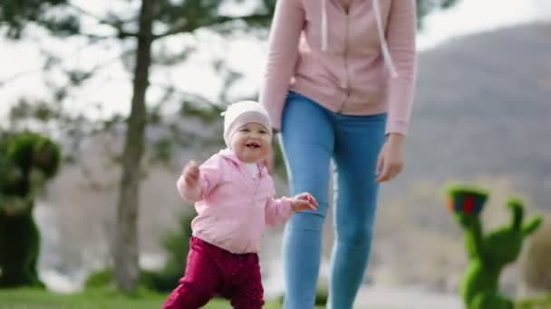 幼い母親は赤ん坊に歩くことを教える 母親と子供が公園を歩く リアルタイムだ 閉じろ — ストック動画