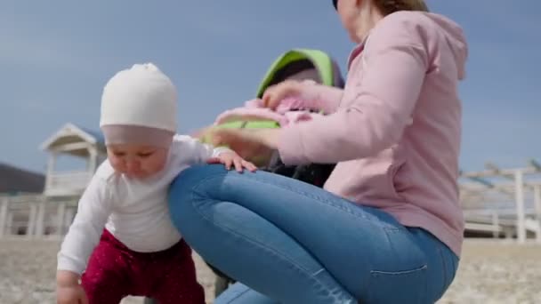 一个可爱的幼儿把鹅卵石捡起来检查 而她的母亲则把她换上其他衣服 儿童节的概念 — 图库视频影像