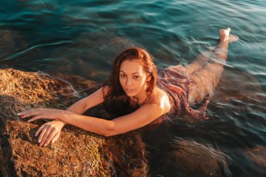 Seksi bronzlaşmış kadın iç çamaşırlarıyla denizde yıkanıyor ve sahil kayalıklarında dinleniyor. Arka plandaki deniz. Yukarıdan görüntüle.