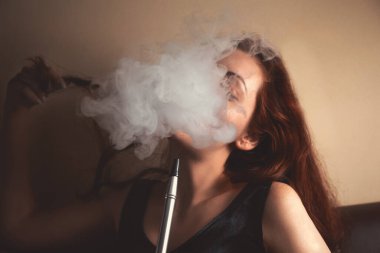 Seksi genç kadın nargile tüttürüyor ve duman bulutunun arkasında yüzünü göremiyor..