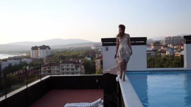 Parlak bir gece elbisesi içindeki zarif sarışın kadın, çatıdaki havuzda geziniyor. İyi akşamlar.