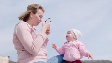 Gülümseyen bir anne küçük çocuğunun güneş gözlüğünü takar. Bebekle oyna. Gerçek zamanlı..
