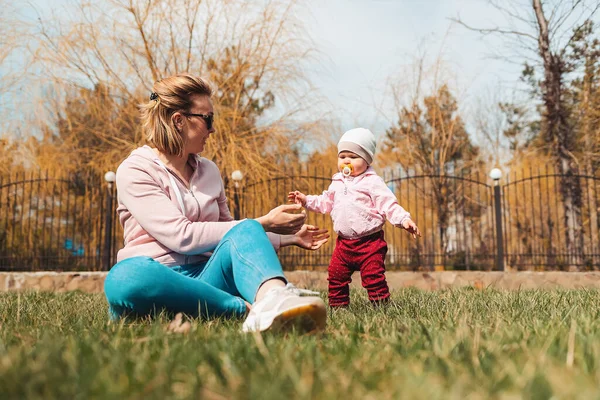 어머니는 풀밭에 앉아서 아기와 줍니다 자녀와 공원에서 가족이 즐기는 — 스톡 사진
