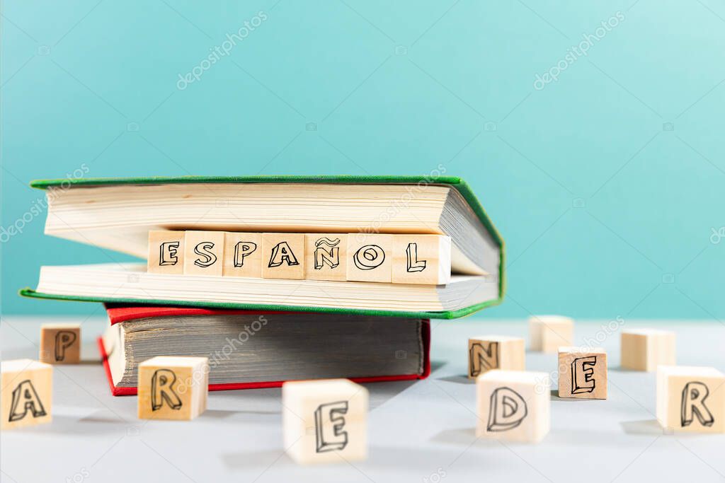 On the table are books and wooden cubes with an inscription in Spanish. Turquoise background. Copy space. The concept of learning foreign languages.