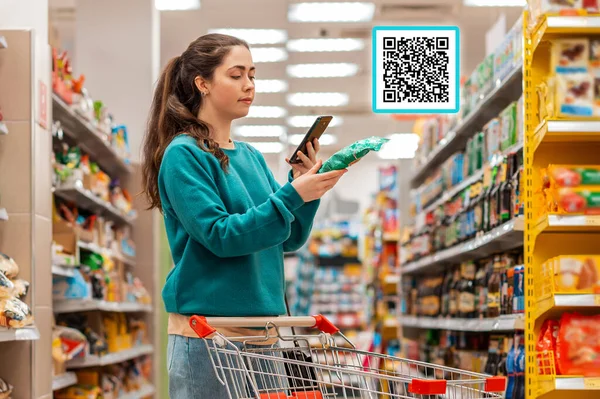 A young beautiful Caucasian woman reads the qr code information using her smartphone. QR-code icon above the product. The concept of purchasing products and mobile apps.