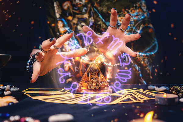 Ведьма колдует волшебную стеклянную пирамиду. Руки крупным планом. Круг Зодиака возле пирамиды. Концепция колдовства и гадания.