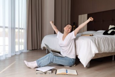 Genç bir kadın dizüstü bilgisayarıyla kucağında oturuyor ve uzun bir antrenmandan sonra esniyor. Online eğitim ve internet sektörü kavramı.