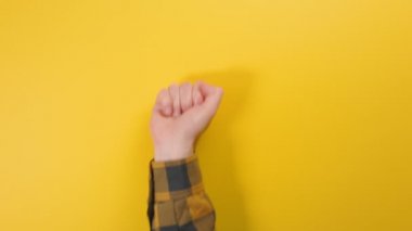 Bir adamın eli aşağıdan belirir ve bir Shaka hareketi yapar. Sarı arka plan. Olumlu jestler kavramı.