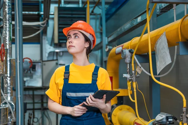 Production inspection. A young engineer in a uniform and a protective helmet, holding a tablet in his hands and conducting an inspection of the equipment. The concept of human equality.