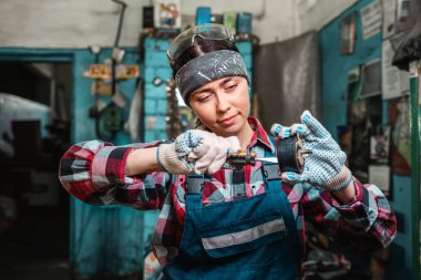 Bir parçayı tornavidayla tamir eden üniformalı genç bir kadın tamircinin portresi. Garajda..