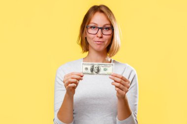 Gözlüklü, gülümseyen bir kadın Amerikan dolarına el koyuyor. Sarı arka plan. Finans ve iş kavramı.