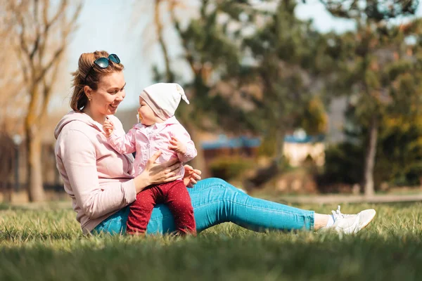 Μια Χαρούμενη Χαμογελαστή Μητέρα Κάθεται Στο Γρασίδι Αγκαλιάζοντας Παιδί Της — Φωτογραφία Αρχείου