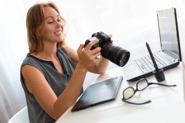 Masasında oturan ve kamerayla çalışan genç bir kadın fotoğrafçı. Kapat..
