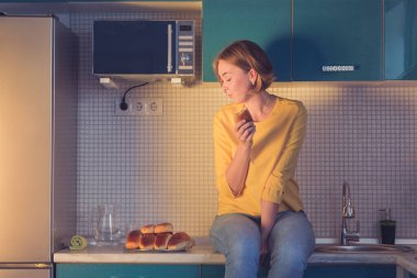 Mutfaktaki masada oturan pastalara zevkle bakan bir kızın portresi..