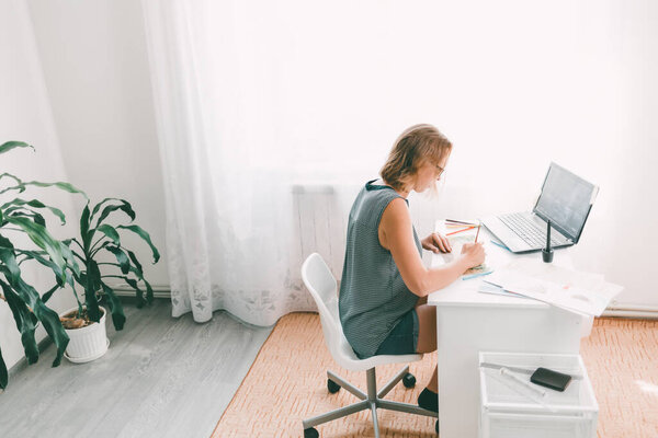 Teacher or speech therapist at work. Young woman with glasses sitting at the table and working with materials for children. Nearby are a laptop and office supplies. Copy space.