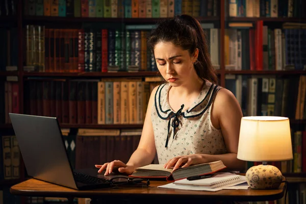 Młoda Biała Kobieta Uważnie Czyta Książkę Pisze Coś Laptopie Stole — Zdjęcie stockowe