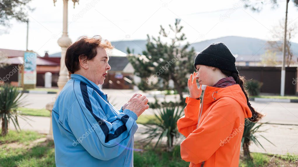 Grandmother scolds the adult granddaughter, standing on the street. Negative communication and problems in the family. Side view.