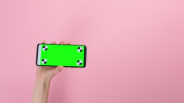 Yatay yeşil renkli anahtar ekranlı cep telefonu tutan bir kadın el. Pembe arka plan. Modern teknoloji ve sosyal medya kavramı.