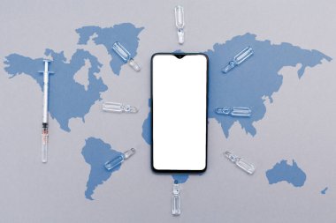 Aşılı ve şırıngalı beyaz telefon ekranı. Dünya haritası olan gri bir arkaplan. Düz yatıyordu. Model yap. Sağlık ve teknoloji kavramı.