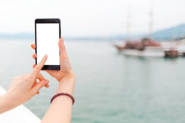 Alay et. Kadının eli telefonu dikey olarak tutuyor ve işaret ediyor. Arka planda, deniz ve gemiler. İzole et.