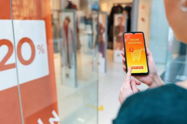 İnternet alışverişi. Bir kadının elinde online bir mağazada açık sayfası olan bir akıllı telefon var. Omzunun üstünden yakın çekim görüntüsü.