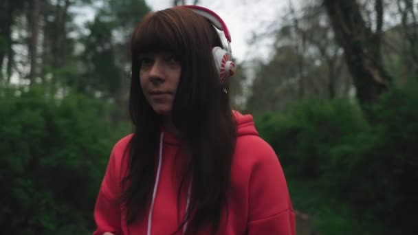 Seorang Wanita Muda Memakai Headphone Mendengarkan Musik Saat Berjalan Taman — Stok Video