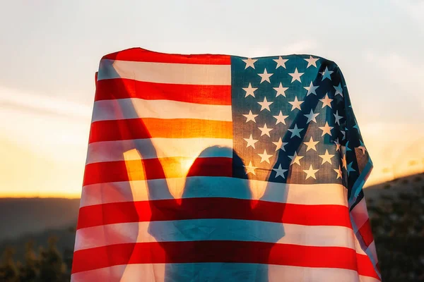 独立日 女人的侧影手里拿着一面美国国旗 高高地高举在头顶之上 后视镜在背景 日落和山脉 美国国定假日的概念 — 图库照片