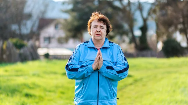 International Day of Older Persons. Portrait of an elderly woman in sportswear doing yoga in a park. Grass in the background. Healthy Lifestyle Concept.