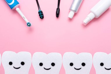 Elektrikli diş fırçası ve plastik diş fırçası, diş macunu ve ağız spreyi ile. Keçeden yapılmış gülümseyen dişler. Düz yatıyordu. Pembe arka plan. Boşluğu kopyala.