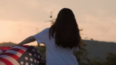 Bir kadın kutluyor ve Amerikan bayrağını sallıyor. Günbatımı gökyüzünün arka planında. Ağır çekim. Arkadan bak. Bağımsızlık Günü Konsepti