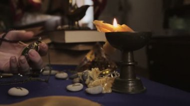 Astroloji ve ezoterizm. Falcı kadın zincirdeki saati açar, kapatır ve yanan mumu üfler. Eller yüzüklere ve bileziklere yakın çekim. Yan görünüm.