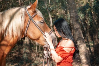 Profilde bir portre. Genç, güzel esmer kadın atı dizginlerinden tutup başını okşuyor..