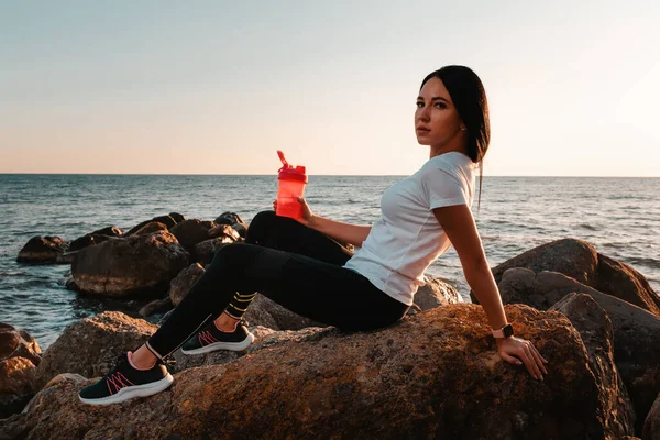スポーツと健康的なライフスタイルの概念 海岸沿いの岩の上に腰を下ろし 握手をしてスポーツウェアを着た女性 スペースのコピー — ストック写真