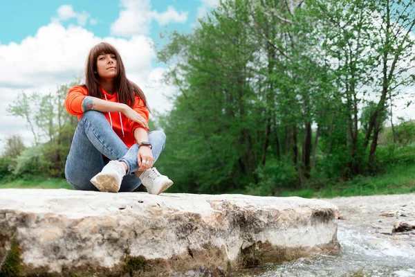 一位年轻的白人妇女坐在河岸的岩石上 底部的观点 公园和室外活动 — 图库照片