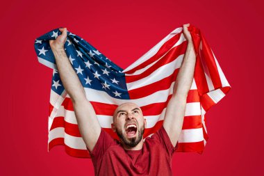 Elinde Amerikan bayrağı olan beyaz bir adam onu kaldırdı ve bağırdı. Kırmızı arka plan. Vatanseverlik, güç, özgürlük ve spor fanatikleri kavramı..