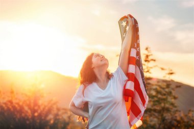Bağımsızlık Günü. Gülümseyen bir vatansever genç kadın elinde bir Amerikan bayrağı salladı. Arka planda gün batımı. Amerikan Ulusal Tatil Konsepti.