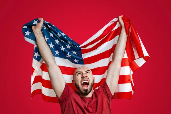 一个手里拿着美国国旗的白人 举起国旗高喊着 红色背景 爱国主义 自由和体育爱好者的概念 — 图库照片