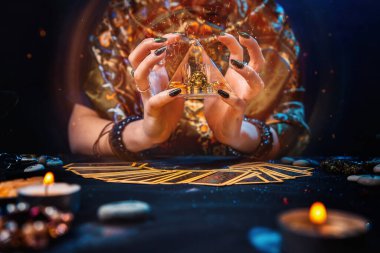 Büyücülük. Cadı elinde parlayan bir piramit tuttu ve onu büyüledi. Tarot kartları masanın üzerindeydi. Eller yakın çekim. Kehanet ve astroloji kavramı.