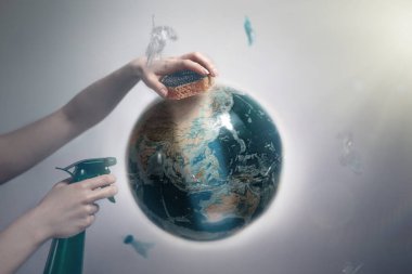 Woman's hand holding a sponge and spray to clear the dirty planet Earth. The concept of improving the state of the environment, Earth Day. Tint and light. clipart