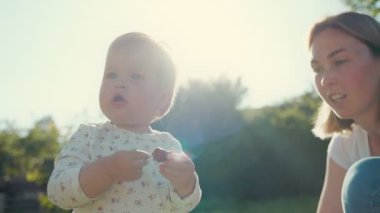 Summertime. A small cute child holds a ripe strawberry in his hands. Real time. The mother smiles and communicates with the child.